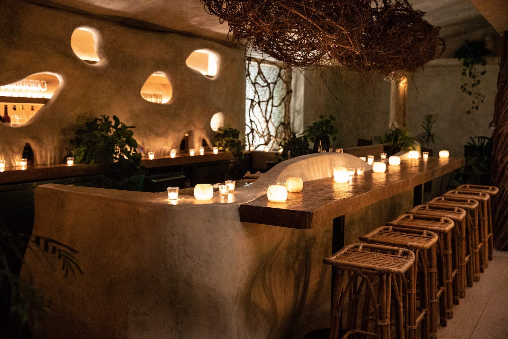The new cocktail lounge at Los Angeles restaurant Meteora with rattan bar stools and a wooden counter with tea lights on it