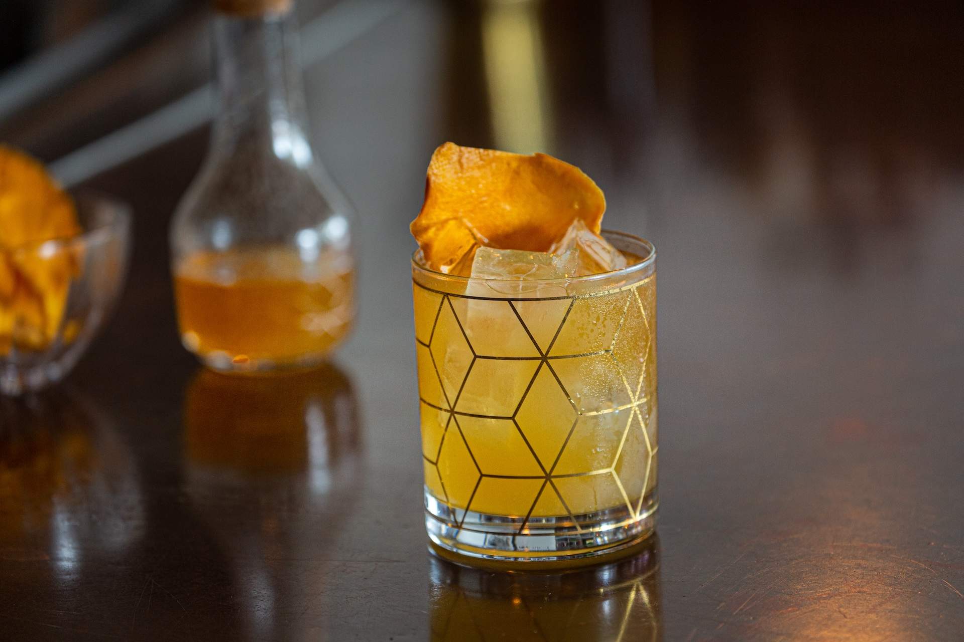A rocks glass containing an orange-colored mango and rum cocktail garnished with a mango peel at Julep in Houston