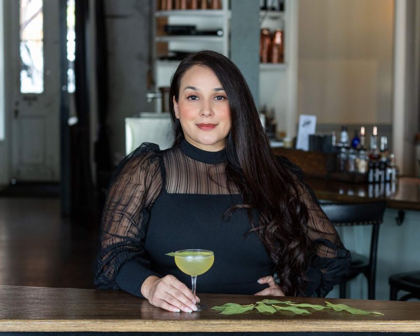Mixologist Alba Huerta stands behind a wooden counter with a clarified gin cocktail at Julep in Houston