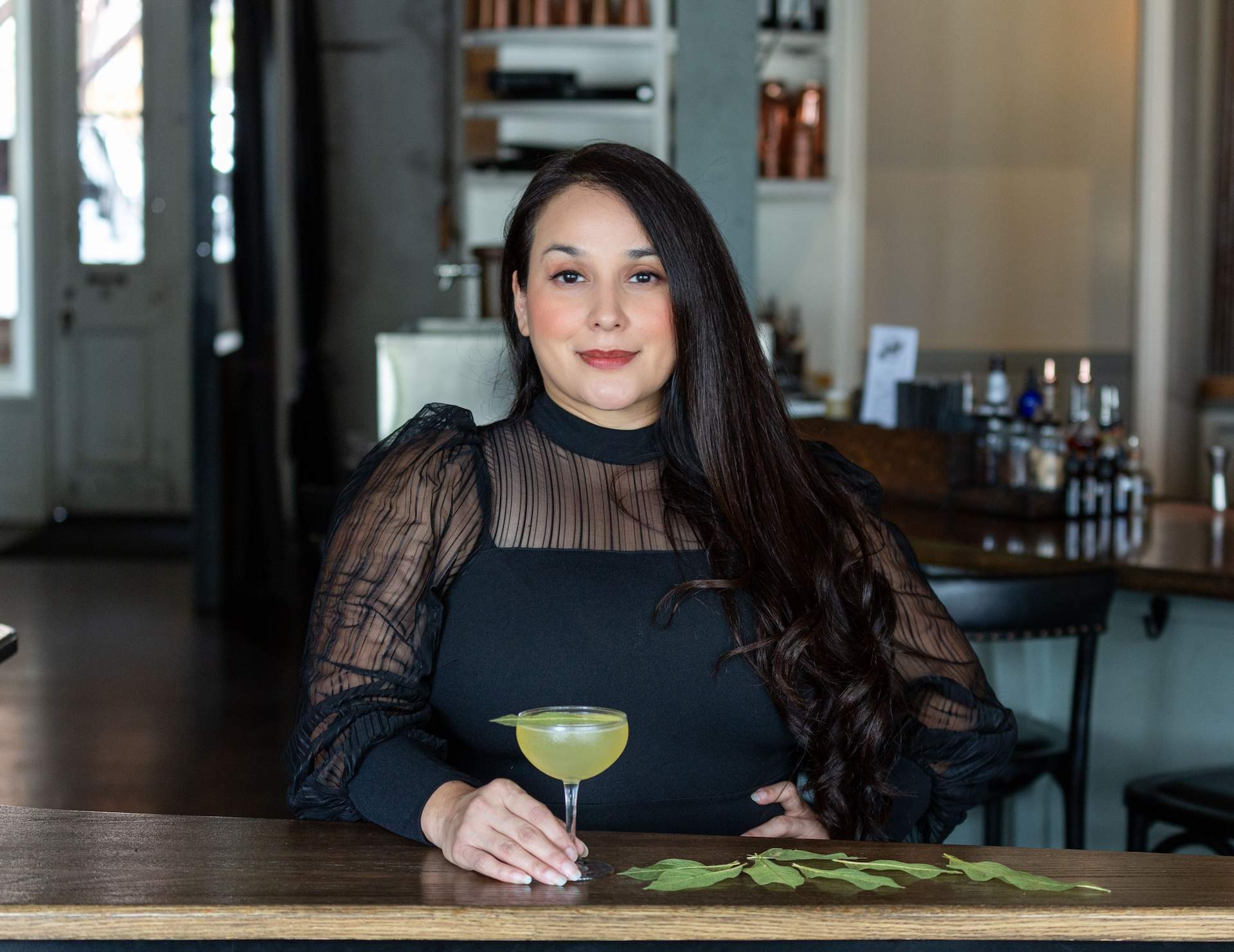 Mixologist Alba Huerta stands behind a wooden counter with a clarified gin cocktail at Julep in Houston