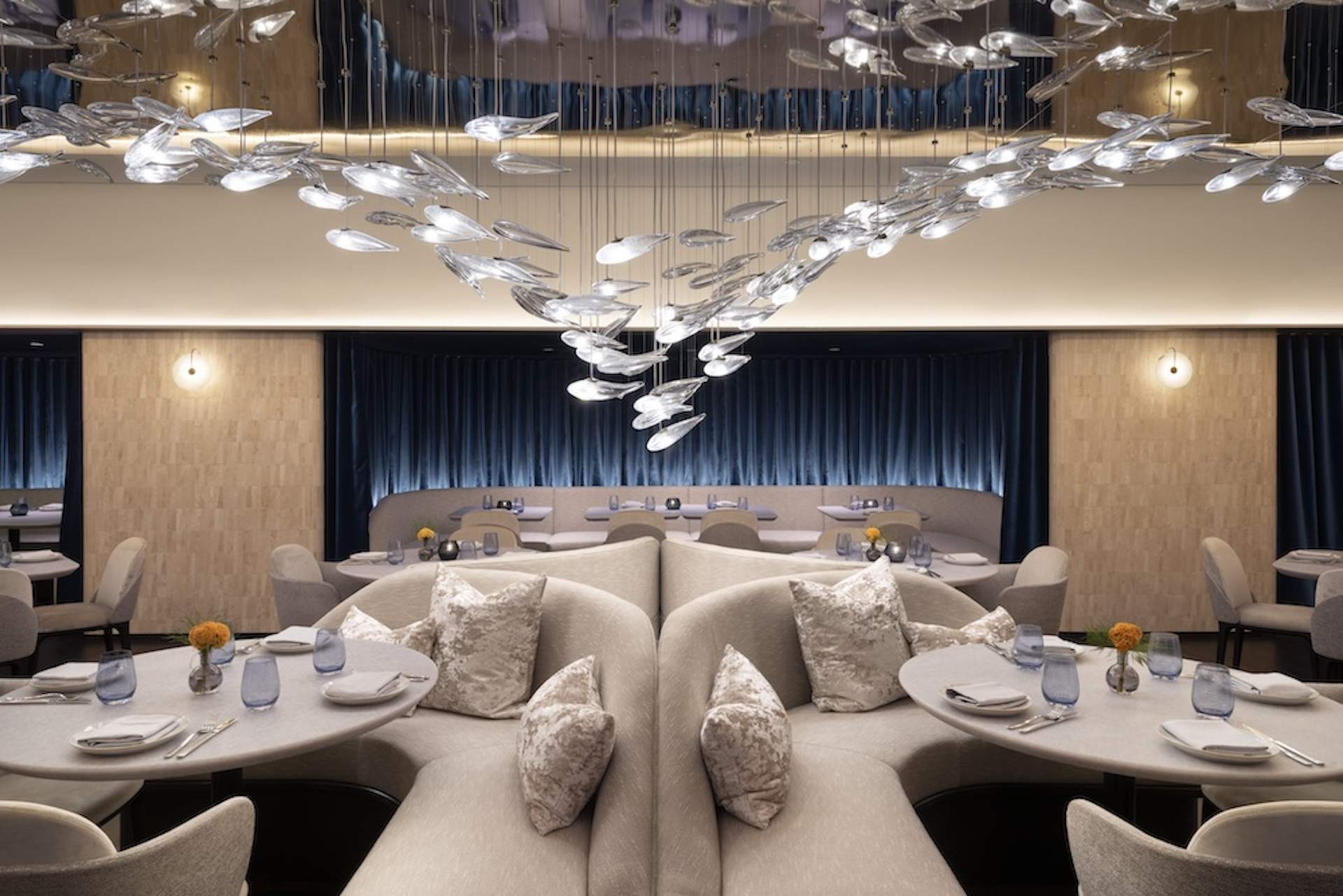 A glass sculpture of lit-up fish seen over seafoam banquettes at NYC restaurant Point Seven