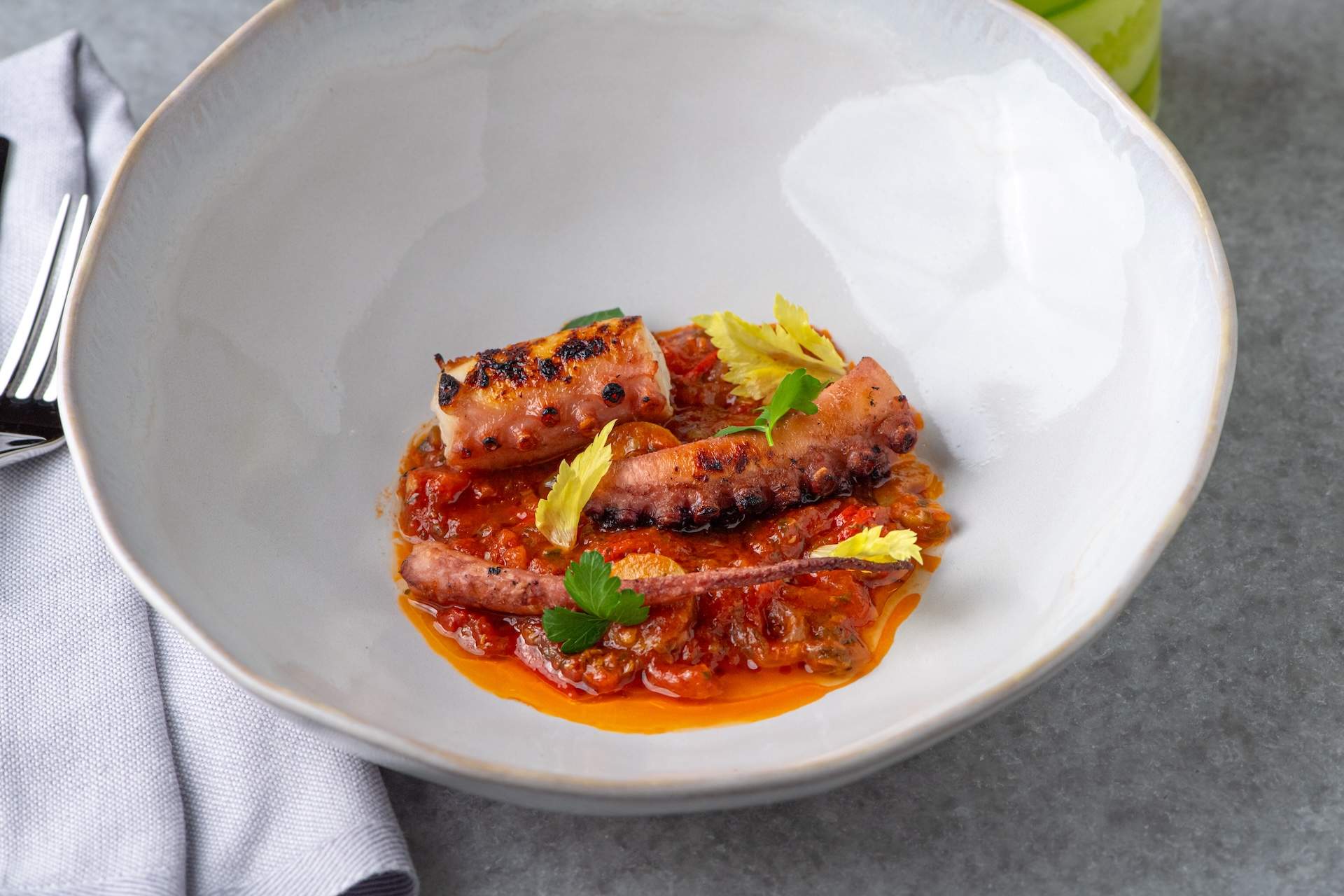 Grilled and cut octopus tentacles sit in a red sauce at NYC restaurant Point Seven