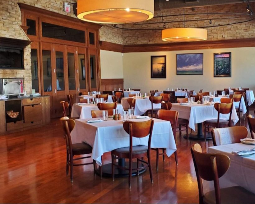 The interior of Northbrook restaurant Prairie Grass Cafe with wooden chairs, white tablecloths, and exposed brick walls