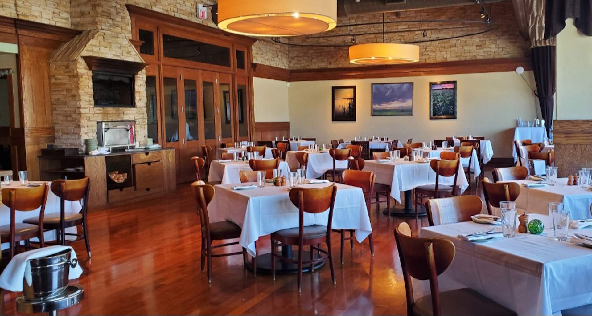 The interior of Northbrook restaurant Prairie Grass Cafe with wooden chairs, white tablecloths, and exposed brick walls