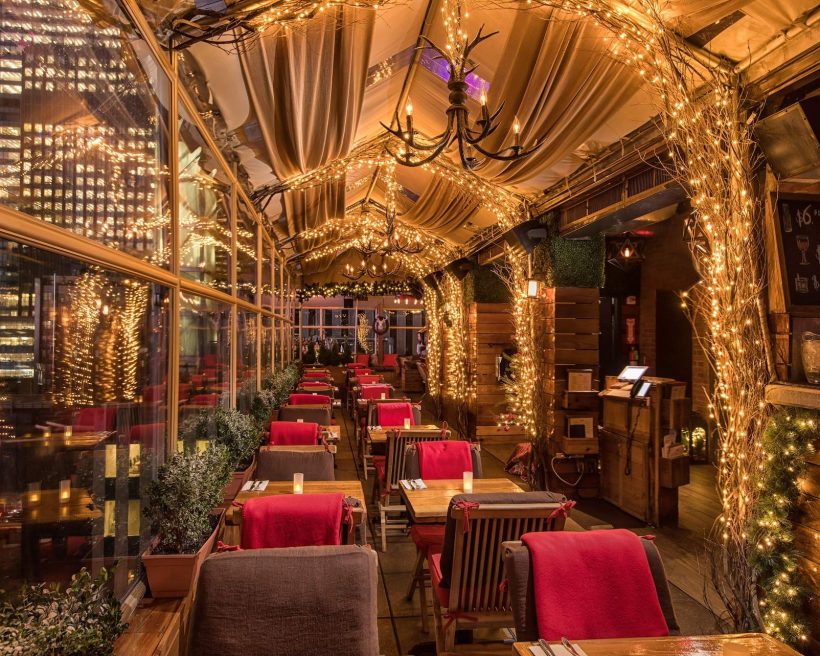 The interior of Haven rooftop at Times Square seen here with a dining room with string lights and wooden chairs draped with red blankets