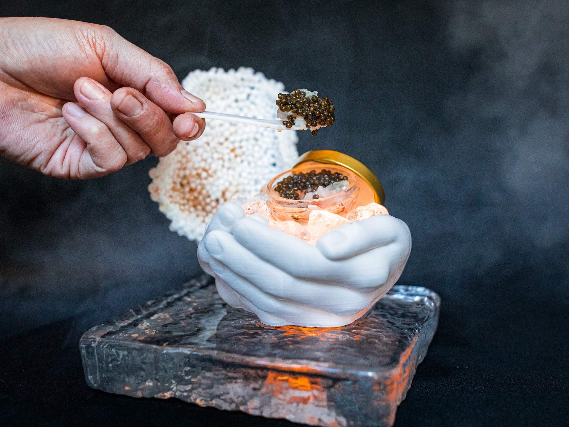 An illuminated plate in the shape of hands cupped together holding a small box of caviar at NYC restaurant Trust Bae
