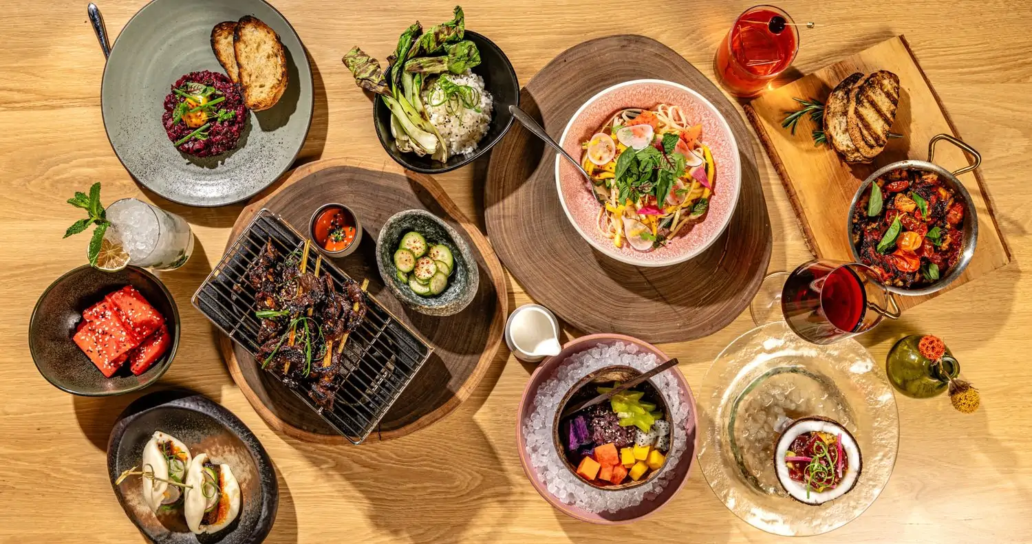 Colorful platters of bao buns, meat skewers, cucumber salad, and other globally-inspired dishes with a glass of wine and ruby-hued cocktail at Wyn Wyn, one of the best new restaurants in Miami on OpenTable.