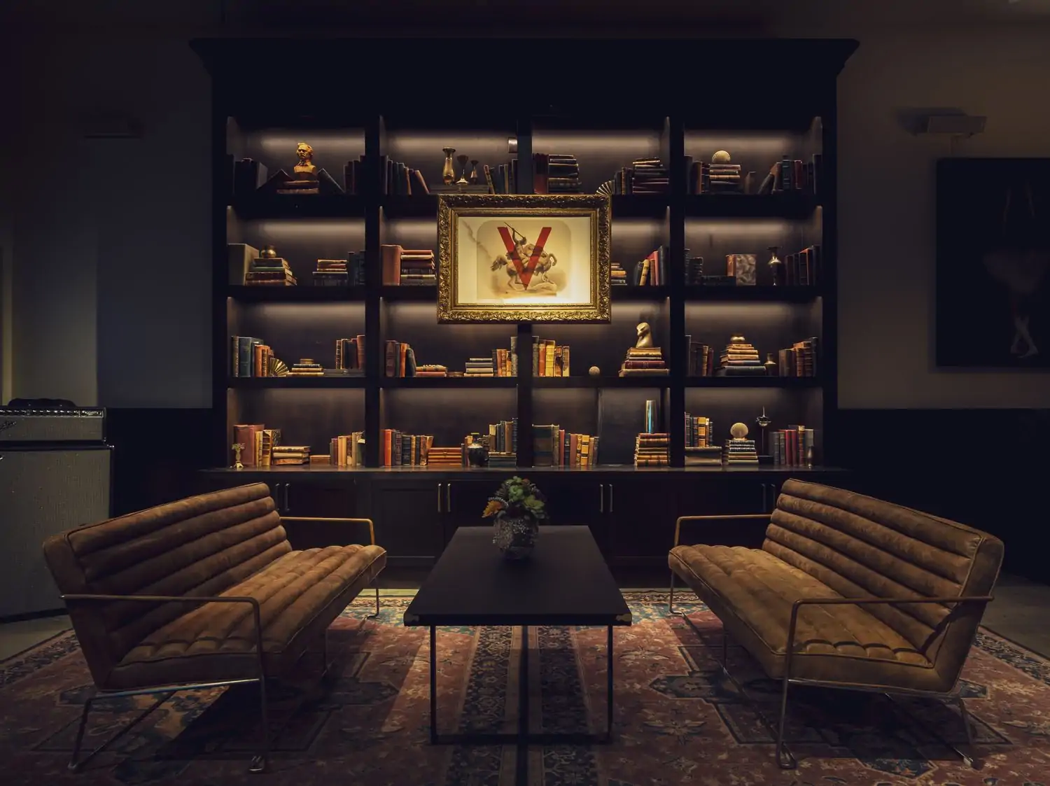 A dark room with a bookshelf full of books and two low-slung sofas and a table at Verse in Los Angeles. Book on OpenTable.
