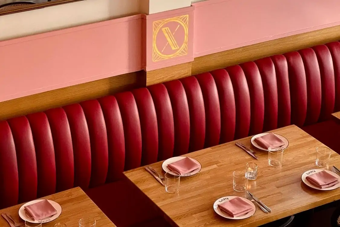 A ruby red banquette set against a candy color pink wall with wooden tables with place settings at Xuntos, one of the most romantic restaurants in Los Angeles for Valentine’s Day on OpenTable.