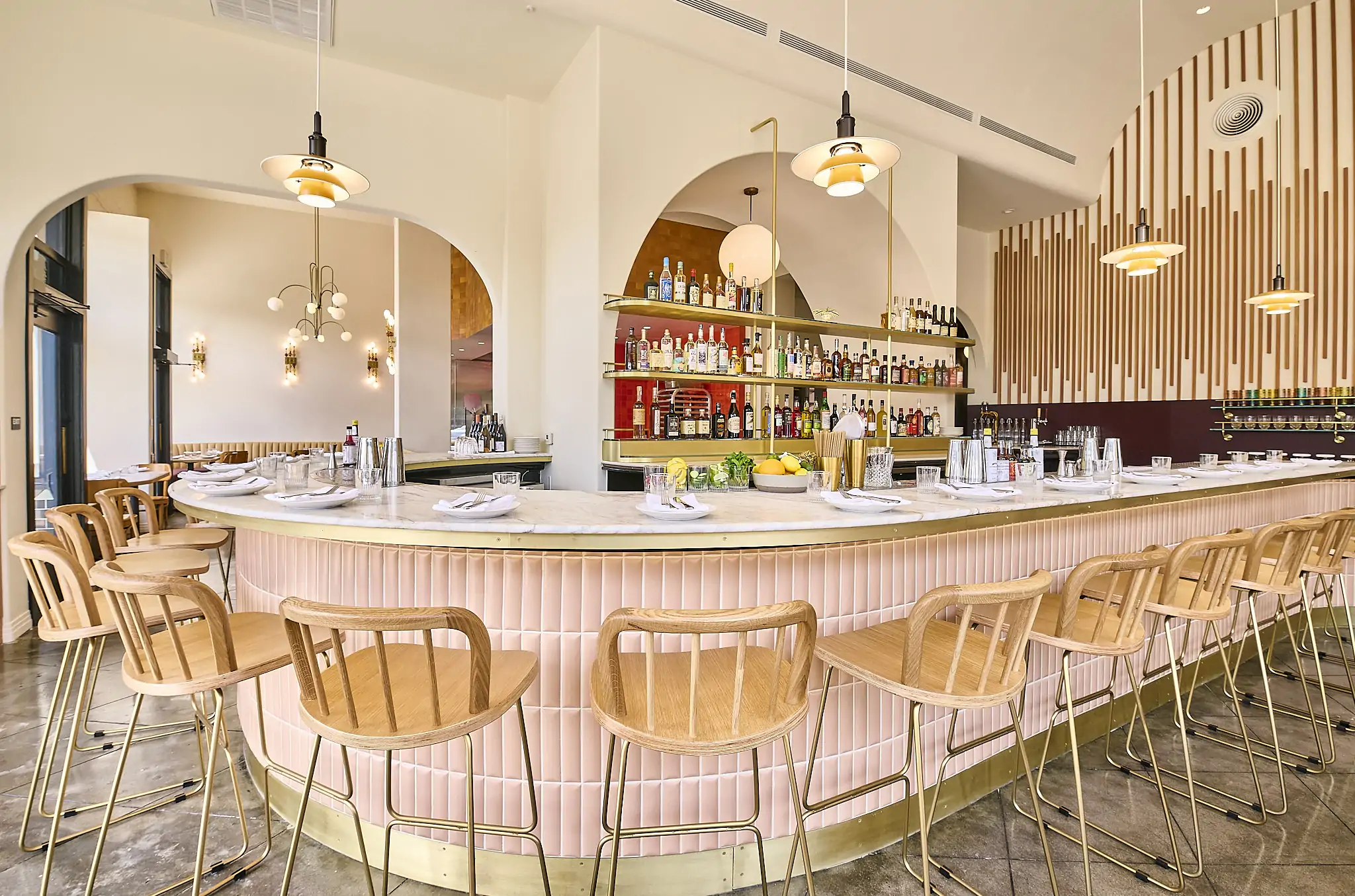 A curved, pink-tiled bar with wooden stools and pendant lights at Saffy’s in Los Angeles. Book on OpenTable.