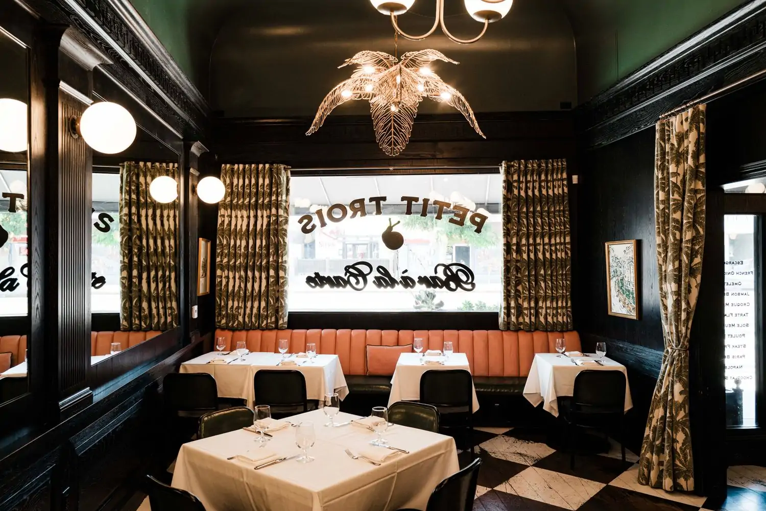 A dark-paneled dining room with peach banquettes, fern-patterned curtains, and tables with white tablecloths at Petit Trois Le Valley, one of the most romantic restaurants in Los Angeles for Valentine’s Day on OpenTable.