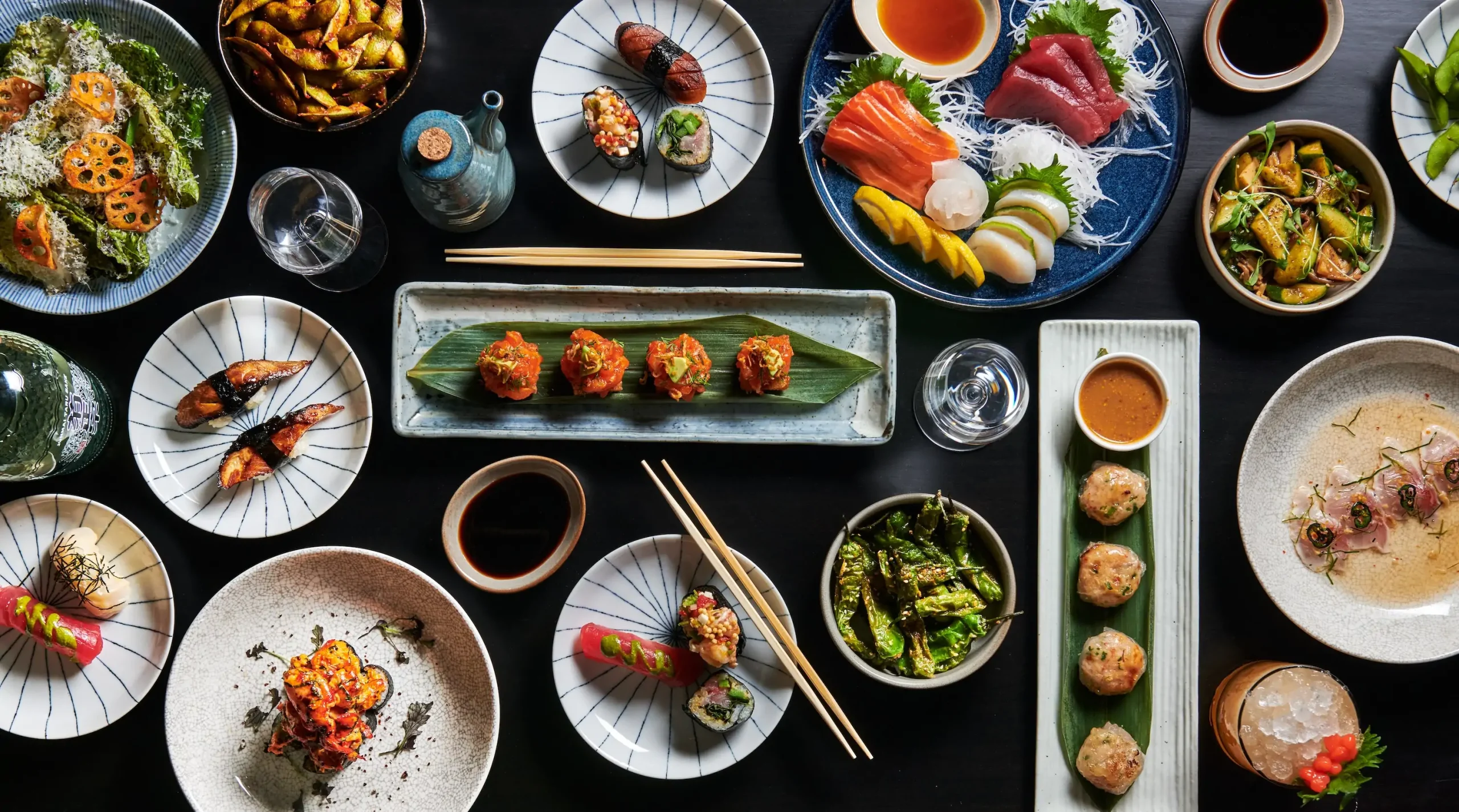 Various Japanese dishes, including sushi, on a black wooden table at NYC restaurant Crave Sushi Bar