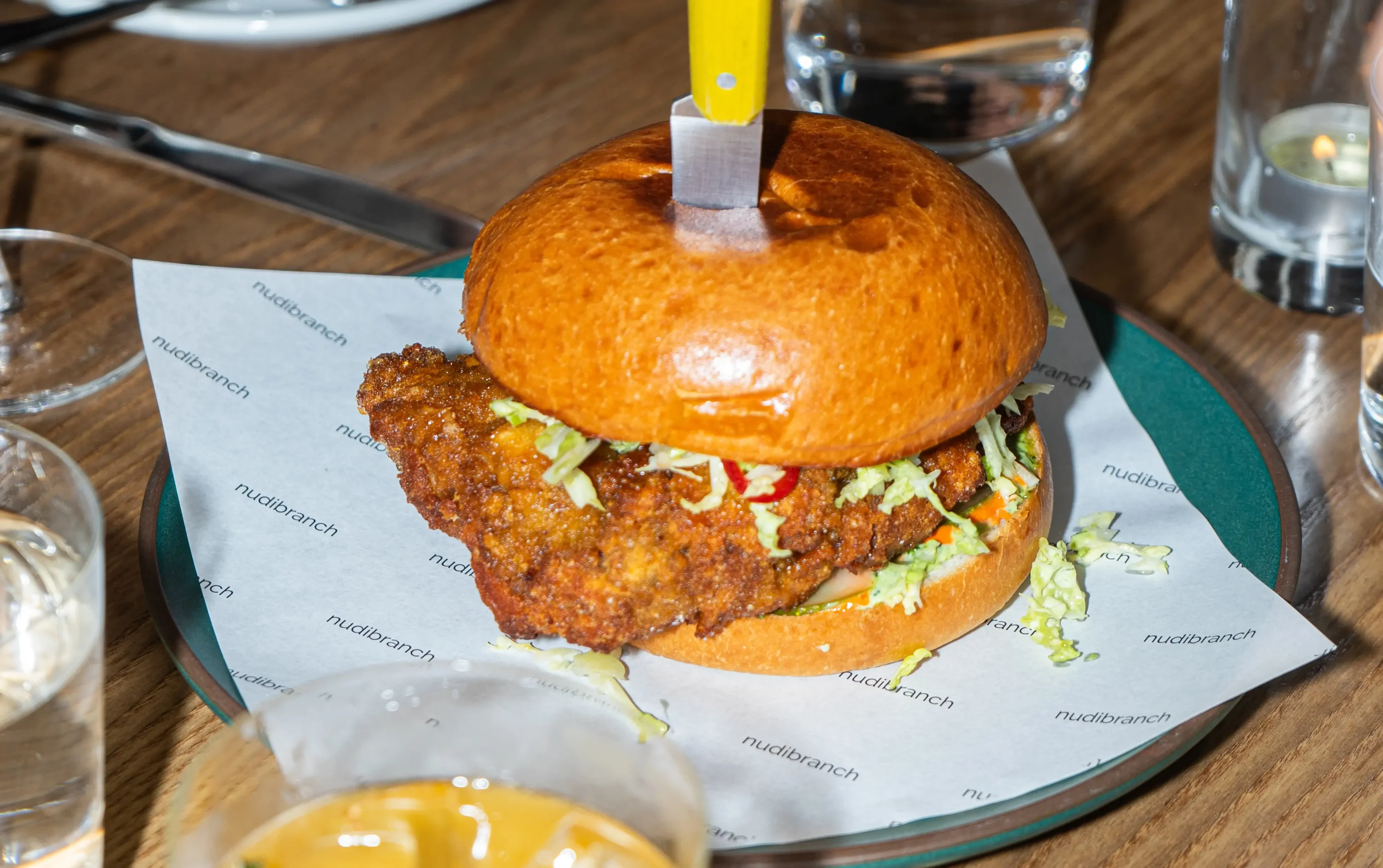 A fried chicken sandwich with a knife skewered in it on top at NYC restaurant Nudibranch