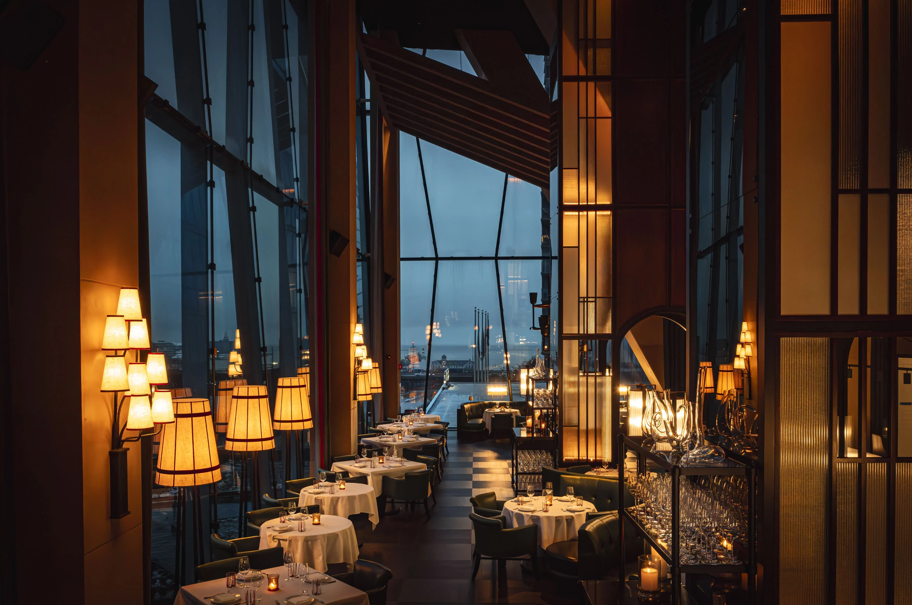 A warmly lit dining room with eight tables draped in white tablecloths. It features high ceilings and views of the city from Tre Dita, one of the best Italian restaurants in Chicago. Book on OpenTable.