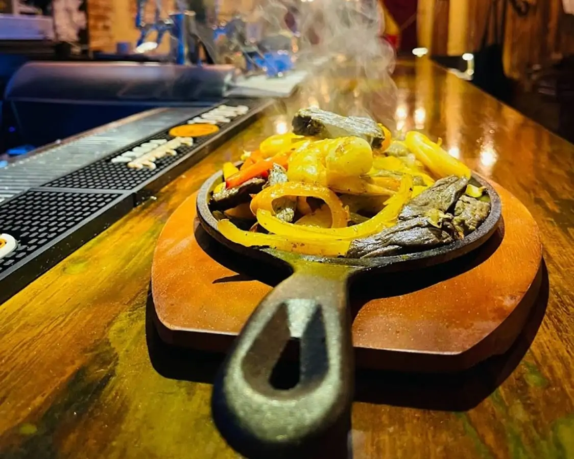 Meat and vegetables sizzling on a cast-iron skillet at NYC restaurant Los Dos Hermanos