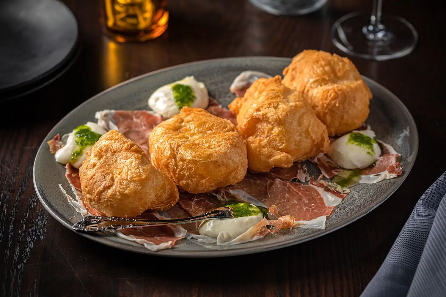 A grey ceramic plate with coccoli, a dish made with stracchino cheese, crispy dough, and prosciutto di parma topped with honey at Siena Tavern, available on OpenTable.