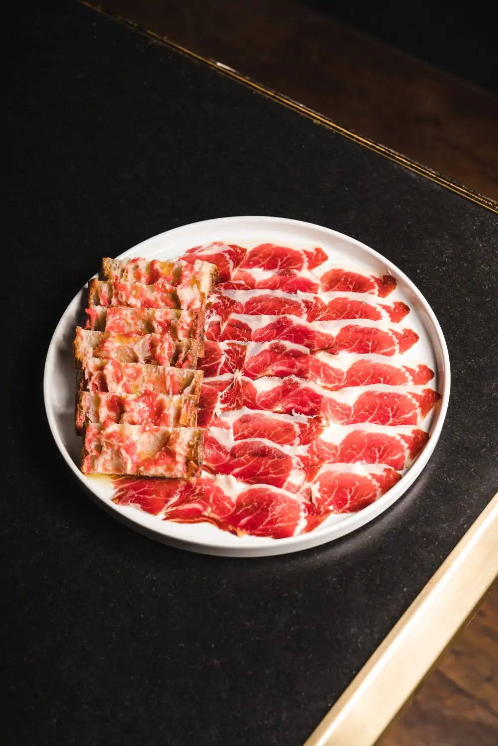 Slices of jamón Ibérico on a white ceramic plate at MAD, one of the fancy restaurants in Houston. Book on OpenTable.
