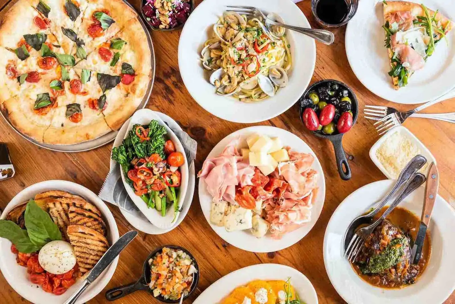 A table setting with Neapolitan-style pizza, cured meats and cheeses, spaghetti alla vongole, and broccoli rabe at Quartino – Chicago, one of the best Italian restaurants in Chicago. Book on OpenTable.