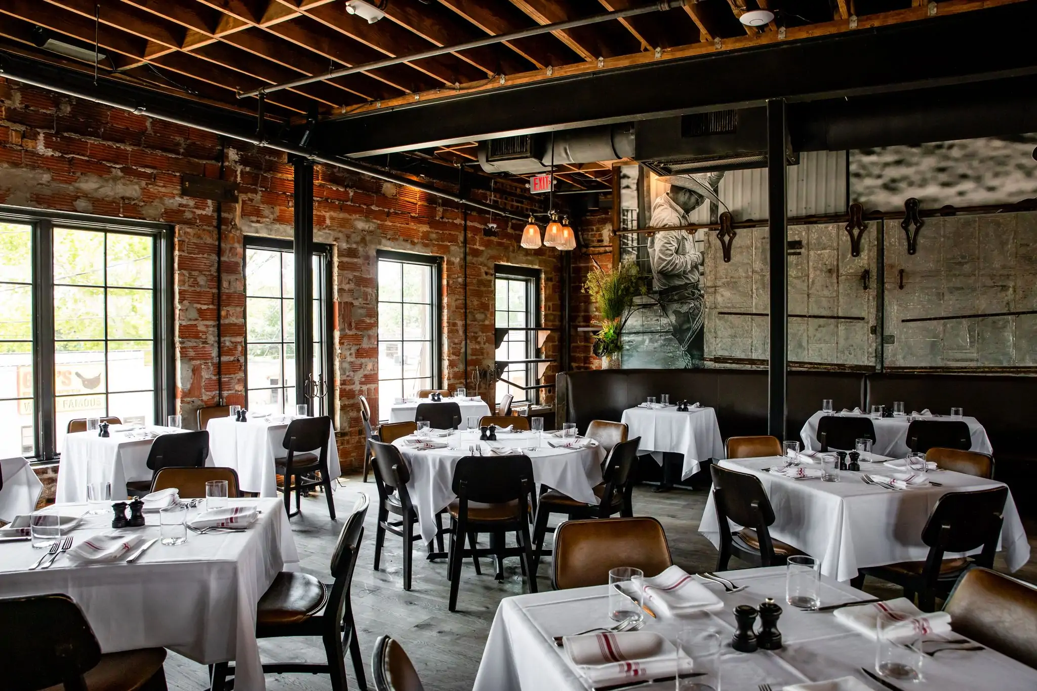Tables with white tablecloths and leather chairs in a dining room with brick walls and industrial accents at B&B Butchers & Restaurants in Houston. Book on OpenTable.