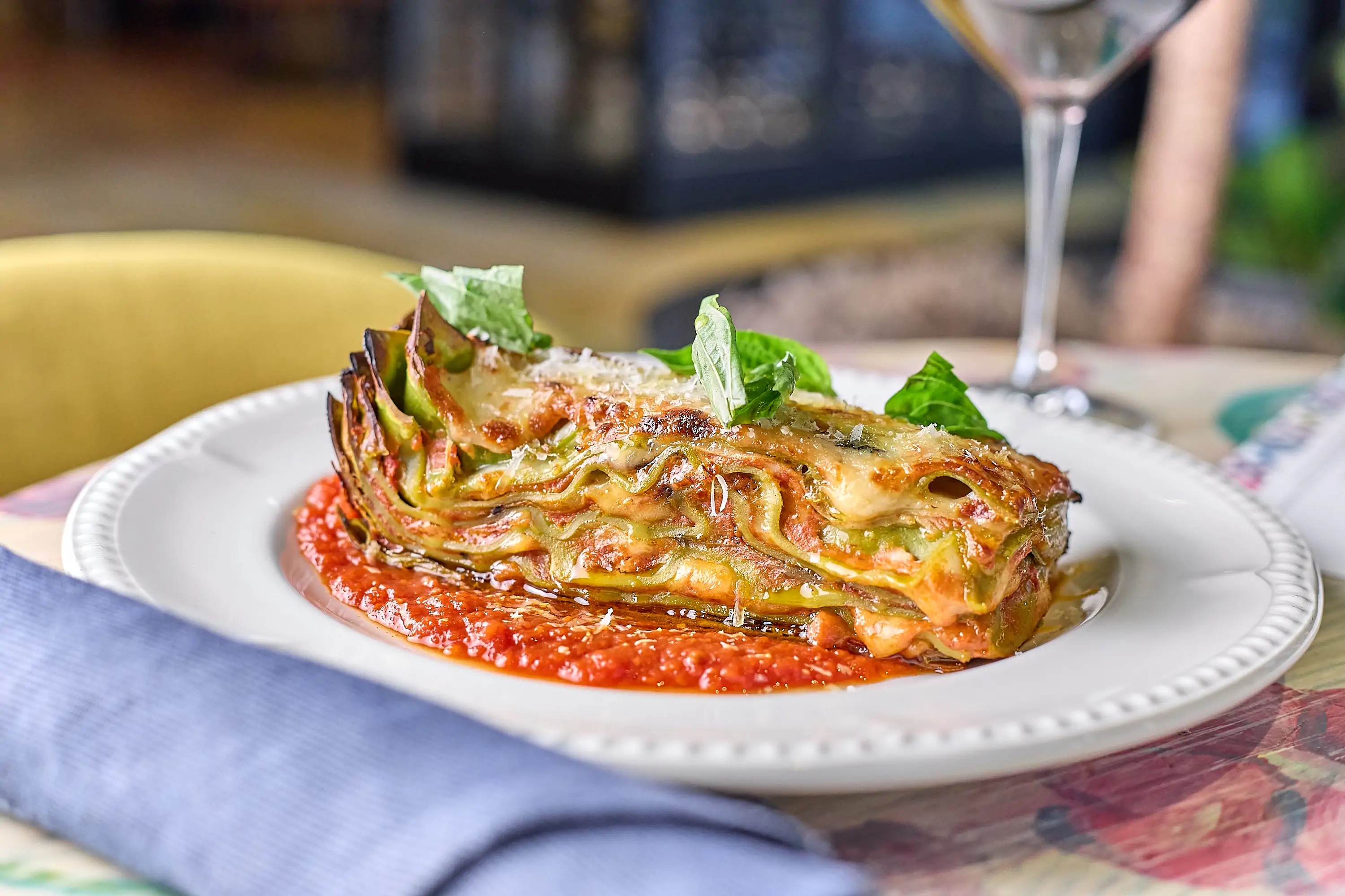 A simple table setting with a large slice of eggplant lasagna and a glass of white wine at Alla Vita, one of the best Italian restaurants in Chicago. Book on OpenTable.