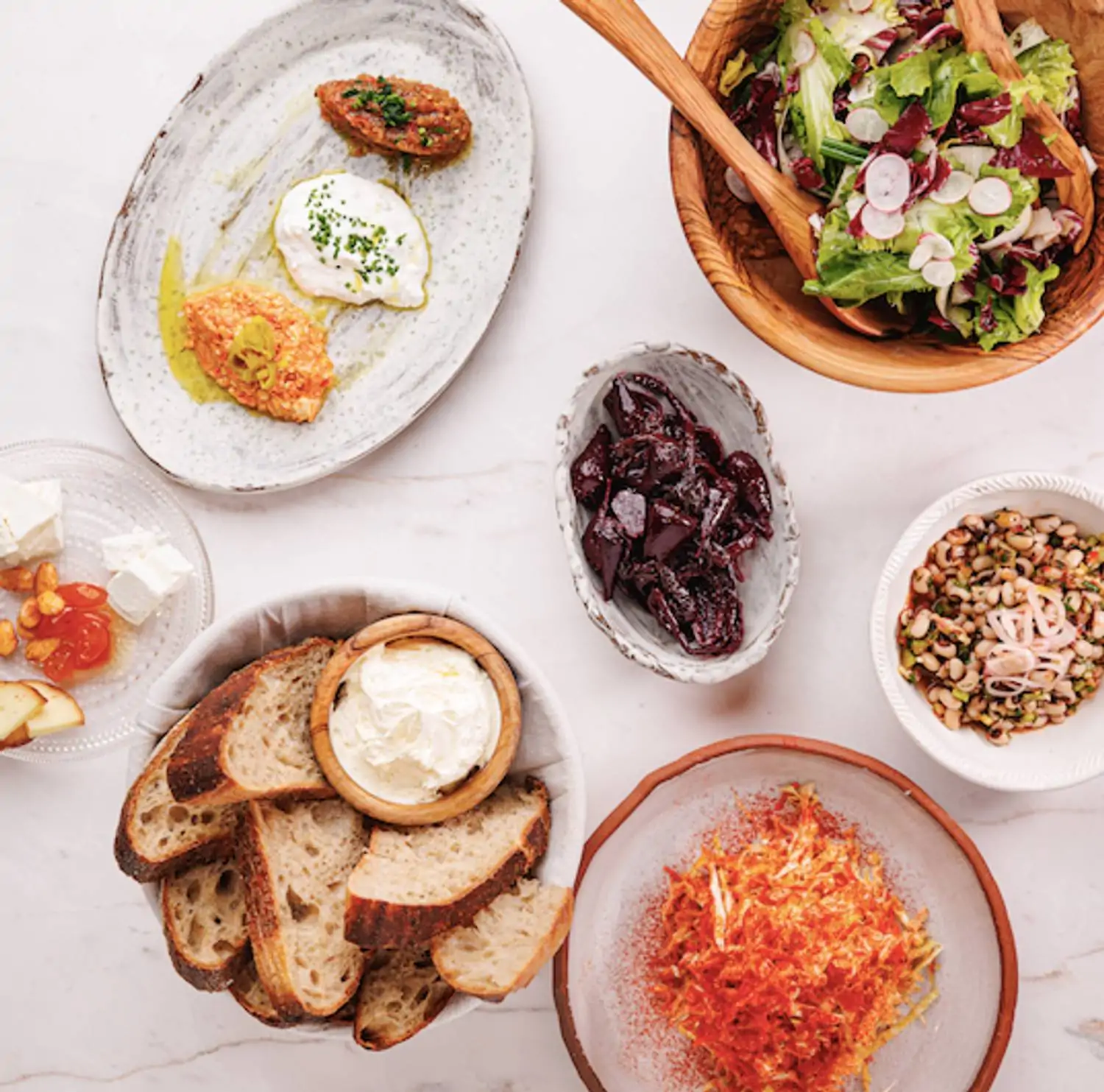 A table with bowls and plates of dips, dates, salads, and other Greek food at Bar Vlaha in Boston. Book on OpenTable.