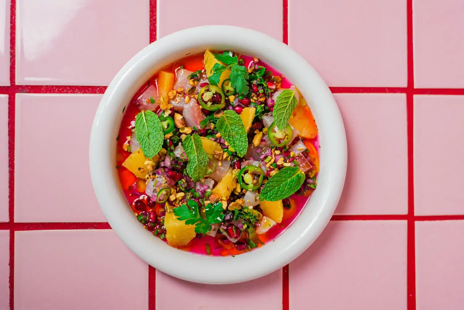 A bowl of ceviche with pomegranates, japaleños, and mint on a pink and red checked background at Ezov, one of the nice restaurants in Austin. Book on OpenTable.
