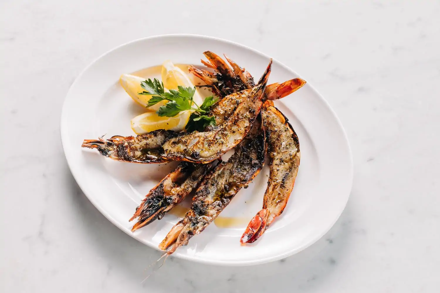 A plate of grilled prawns cut in half and three slices of lemon at RPM Italian – Chicago. Book on OpenTable.