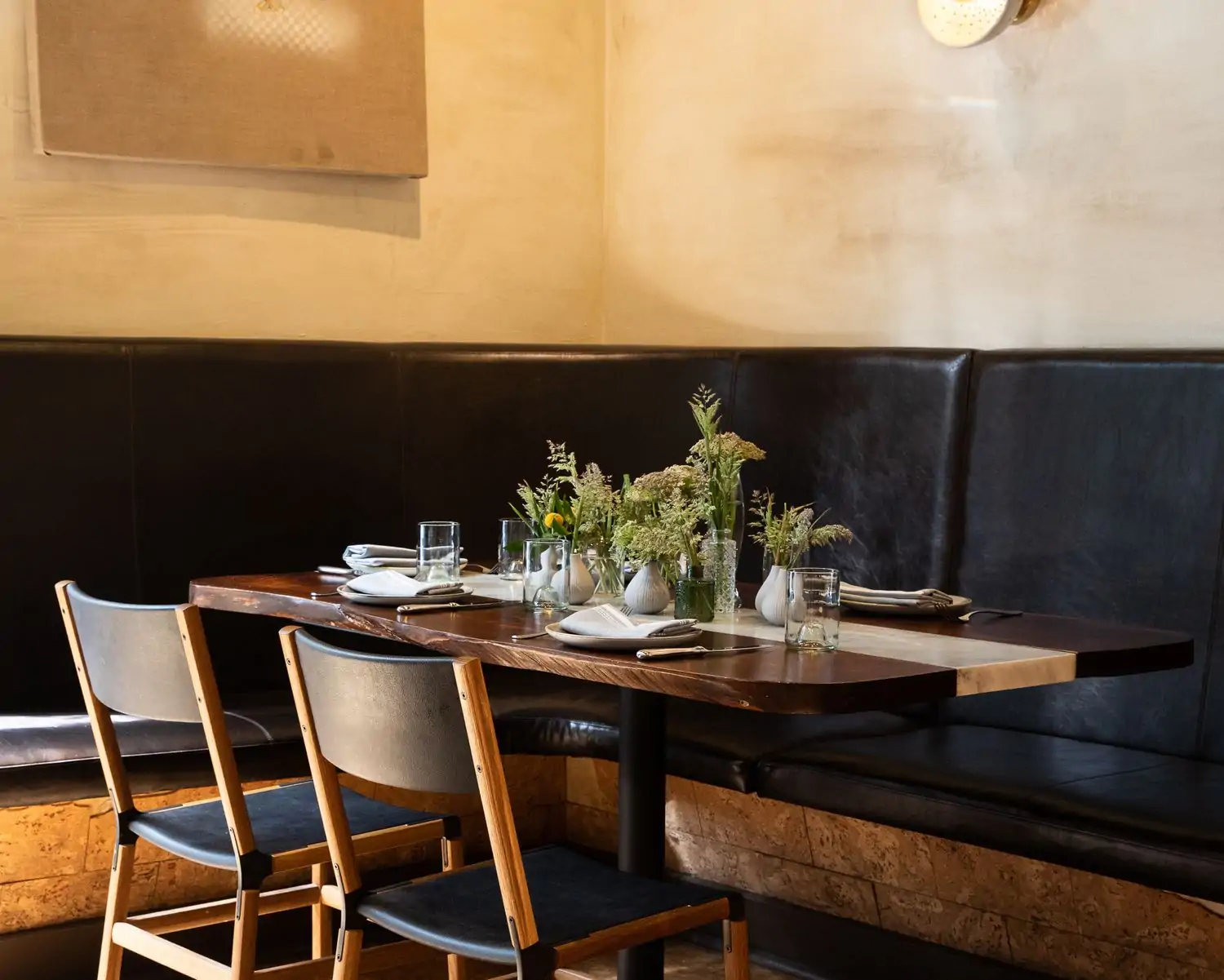 A corner table in a bright restaurant with black booths and chairs in front of a table setting with flowers at A16 San Francisco.