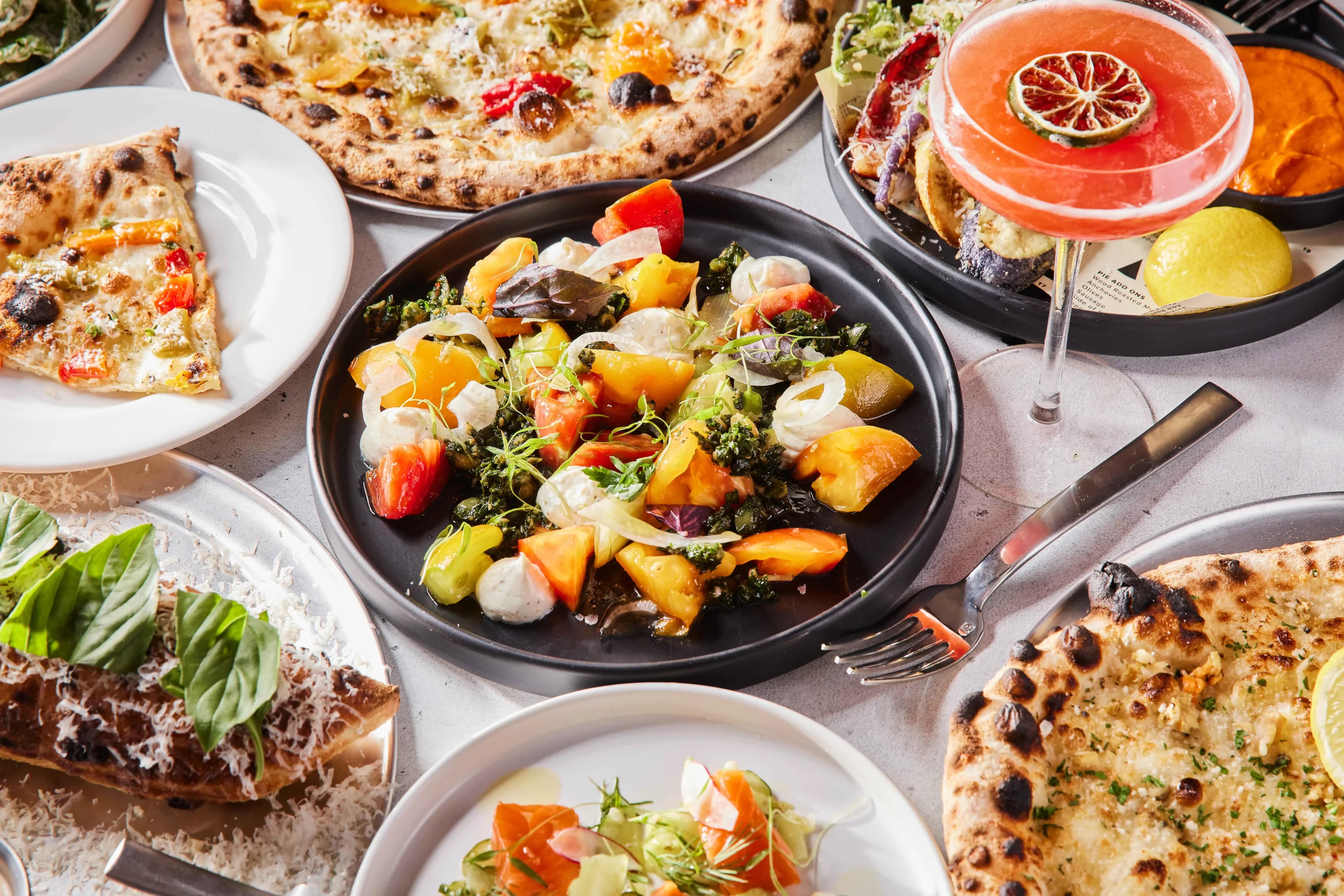 A table with different pizzas surrounding a plate of antipasti salad at Fiorella in SF, available on OpenTable.