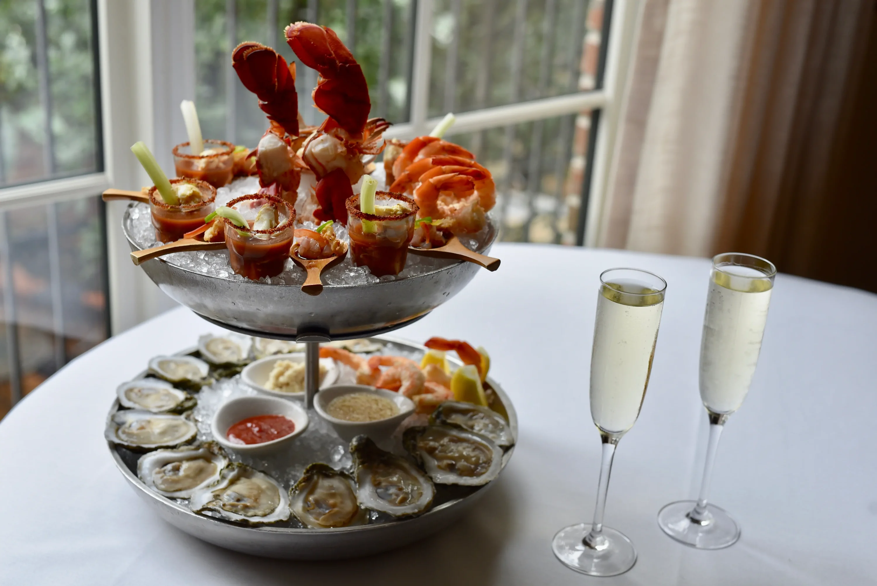 A platter of oysters, shrimp, and other raw foods on a platter and two glasses of sparkling wine at Brennan’s of Houston, available on OpenTable.