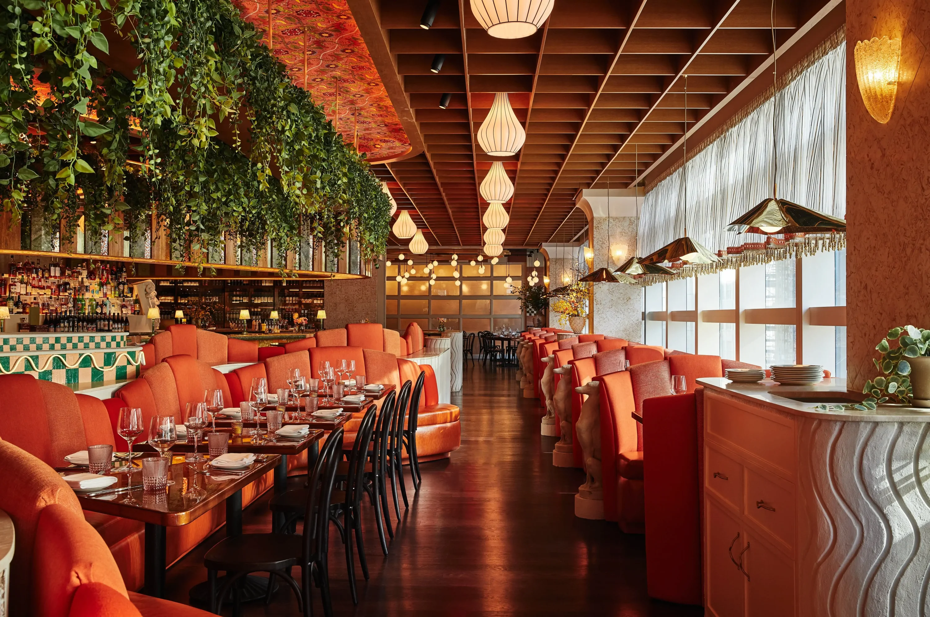A modern dining room with red booths, hardwood floors, and decorative lighting at Bad Roman, one of the best Italian restaurants in New York City. Book on OpenTable.