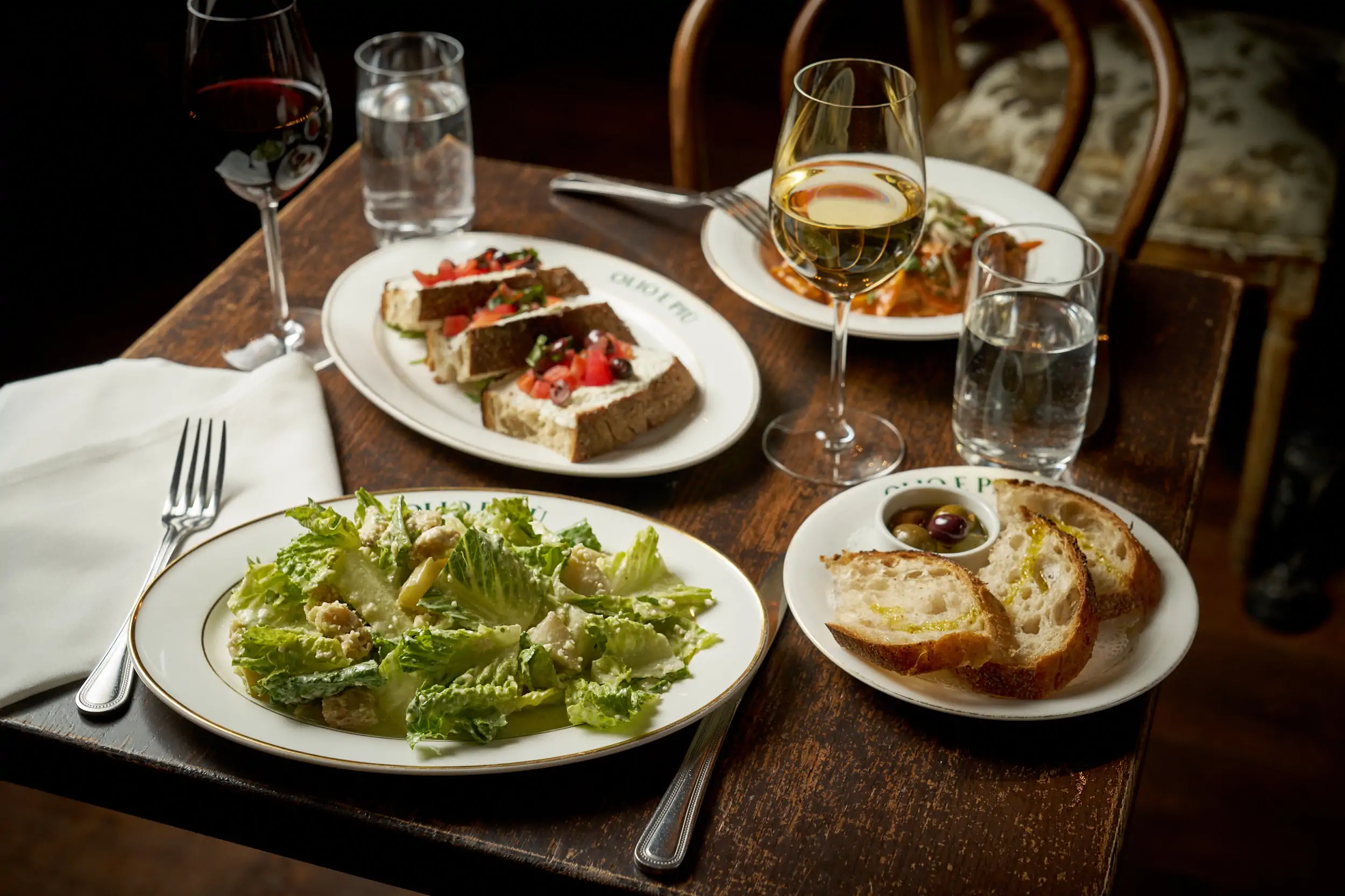 A table with bruschetta, bread, and salad served alongside wine at Olio e Più, one of the best Italian restaurants in New York City. Book on OpenTable.