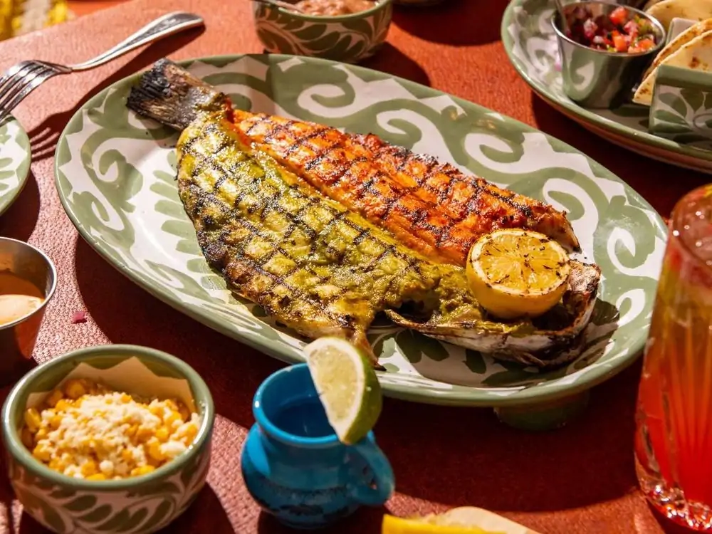 A plate of grilled branzino fish surrounded by other items in a vibrant table setting at The Hideaway, one of the best restaurants in Los Angeles, Beverly Hills.
