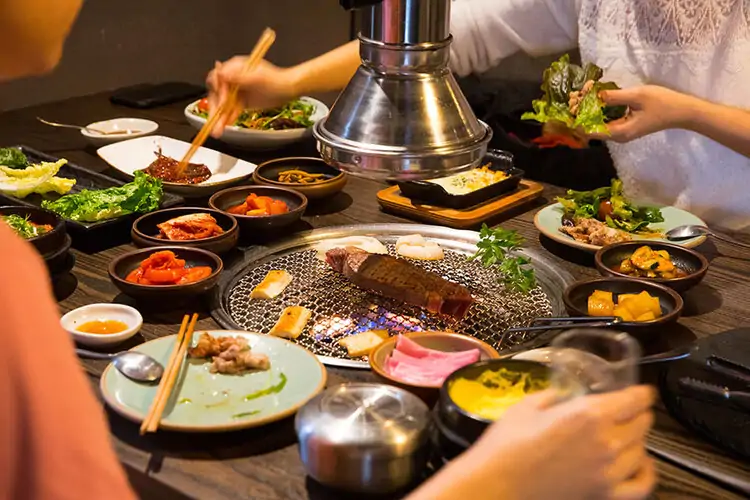 Various cuts of meat on a table grill surrounded by vegetable side dishes at BORI in Houston, available on OpenTable.