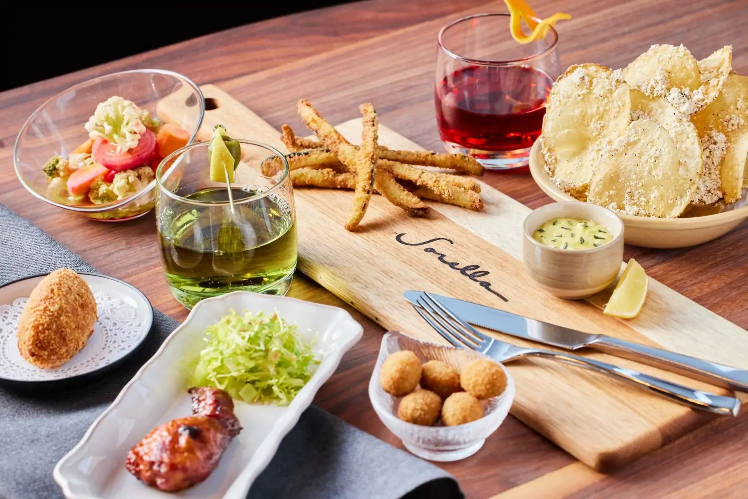 A spread of appetizers including salad, chips, and chicken wings, on a Sorella cutting board at one of the best Italian restaurants in San Francisco.