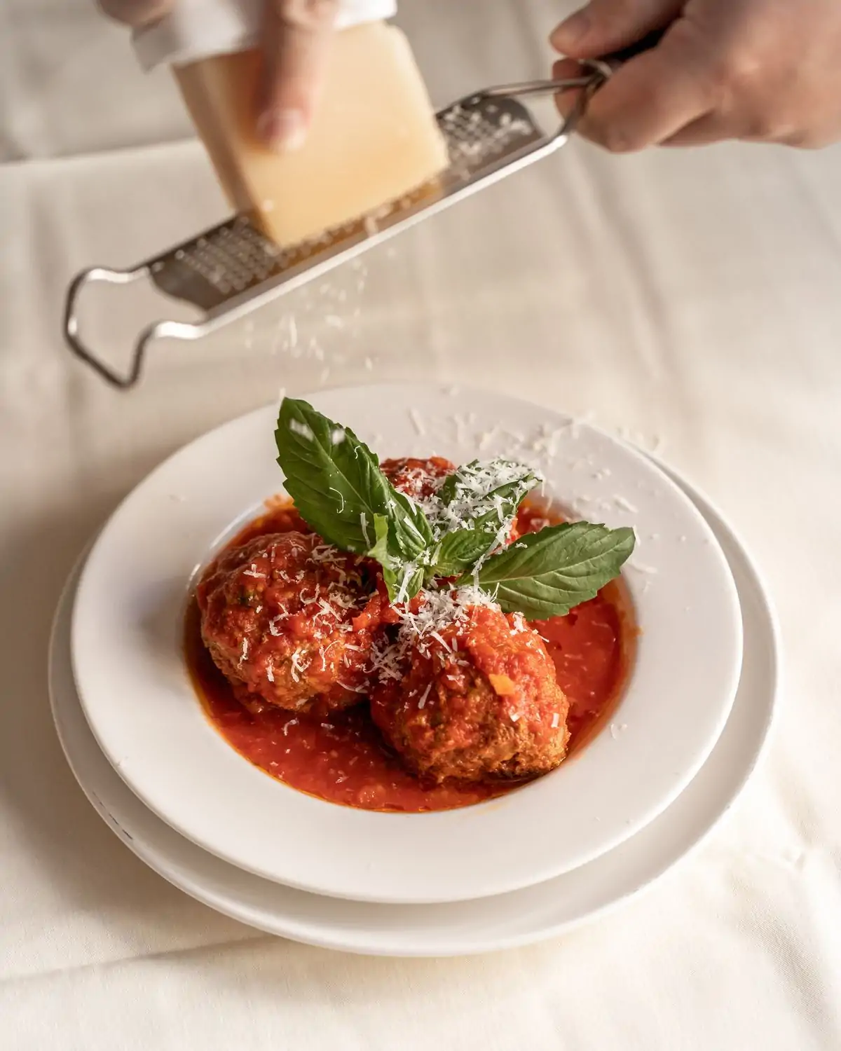 A bowl of Italian meatballs with the waiter shredding cheese on top at Becco, one of the best Italian restaurants in New York City. Book on OpenTable.