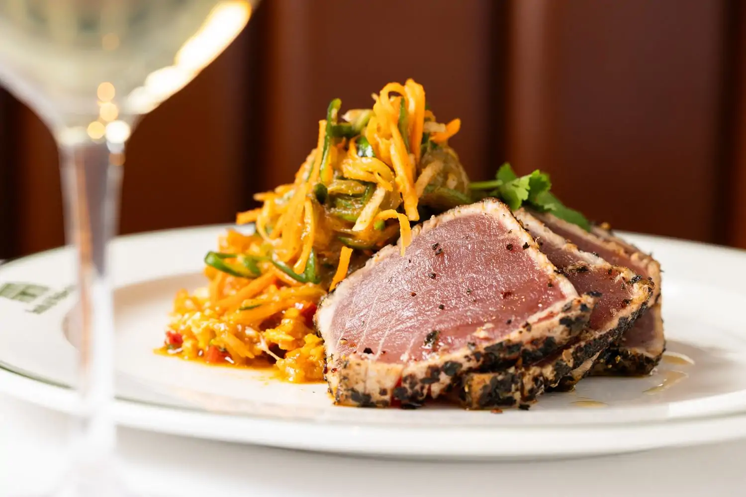 A plate of seared tuna with a shredded carrot salad and a glass of white wine at Smith & Wollensky Steakhouse – Miami, one of the best restaurants in Miami Beach, on OpenTable.