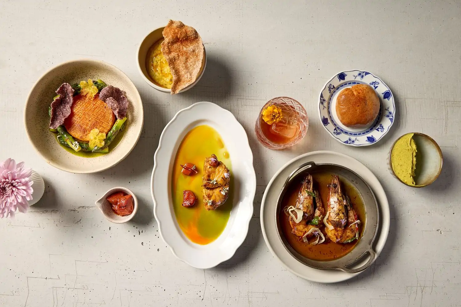 A sparse concrete table with six minimalist and modern Indian dishes plus one whiskey-based cocktail in an etched glass tumbler at Baar Baar, one of Los Angeles’ best Indian restaurants you can book on OpenTable.