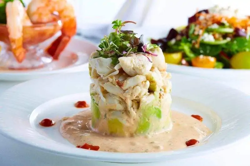 Topped with greenery, a tower of flaky white morsels of seafood rests in creamy pale orange sauce at OpenTable selection, Café Pacific, one of the best restaurants in Dallas.