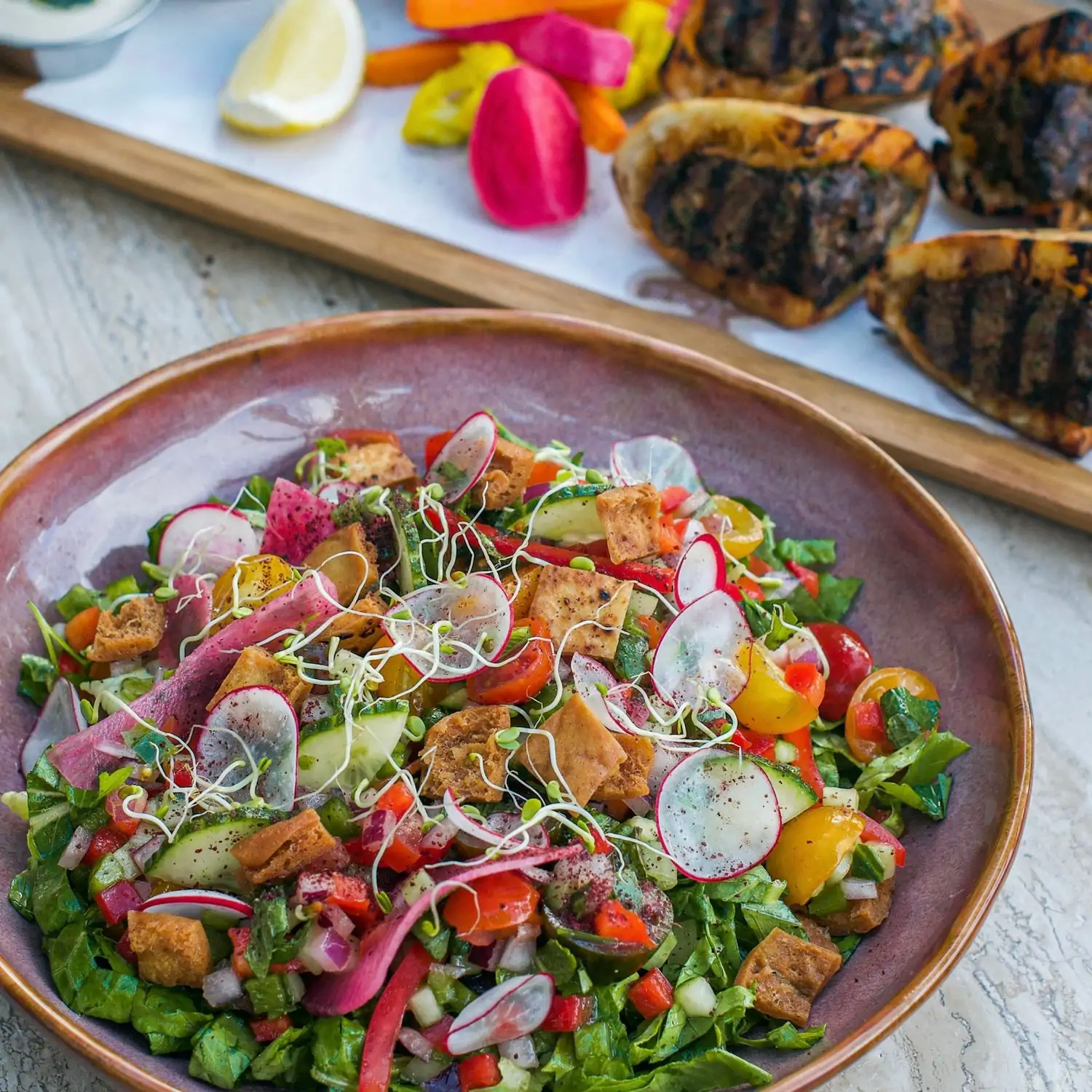 An earth-toned ceramic plate with a fattoush salad and offerings from the grills in the background at Abbalé Telavivian Kitchen - South Beach, one of the best restaurants in Miami Beach, on OpenTable.