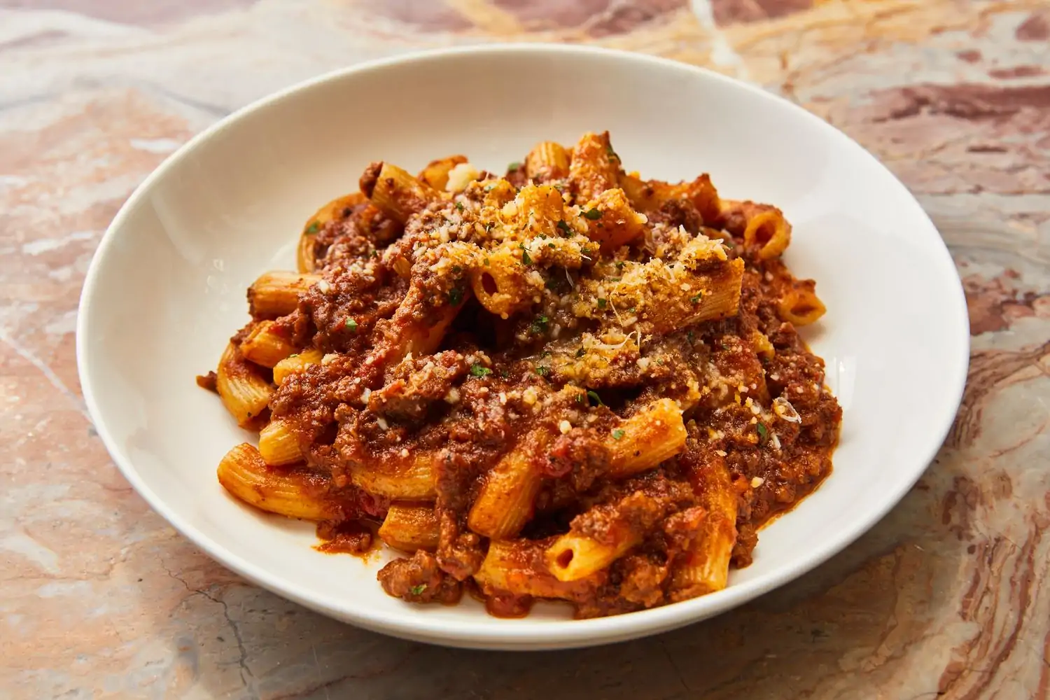 A marble table holds a white plate with rigatoni beef bolognese and grated parmigiana at Cecconi’s, one of the best restaurants in South Beach Miami. Book on OpenTable.