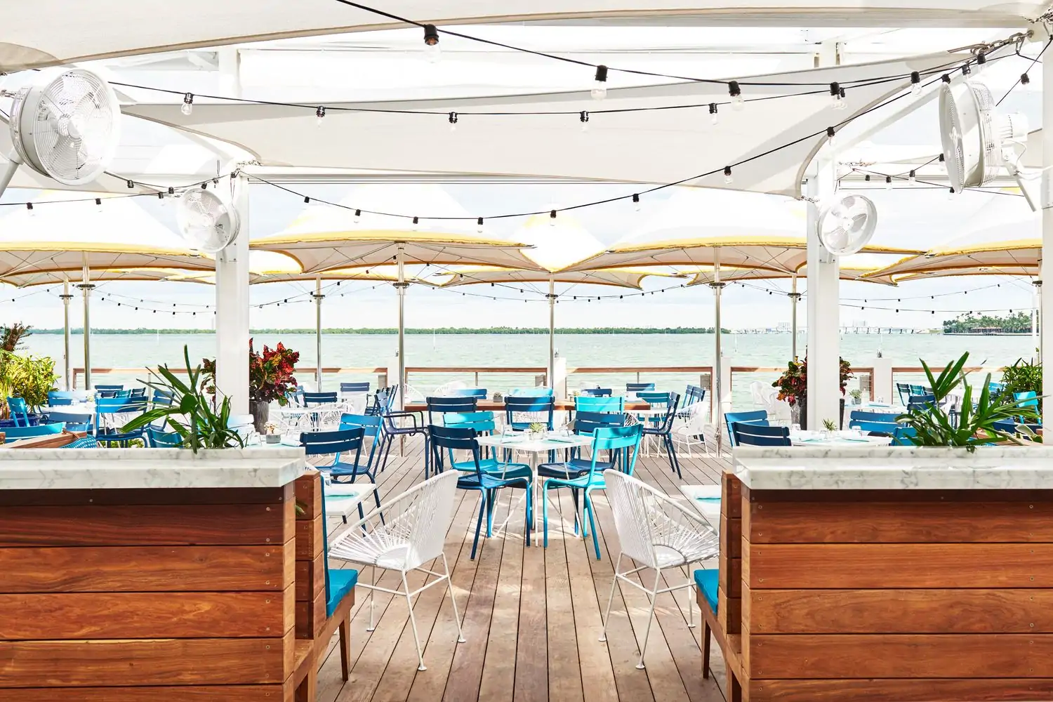 Blue and white chairs underneath umbrellas and string lights next to the bay at Lido Bayside Grill at The Standard Spa in Miami Beach. Book on OpenTable.
