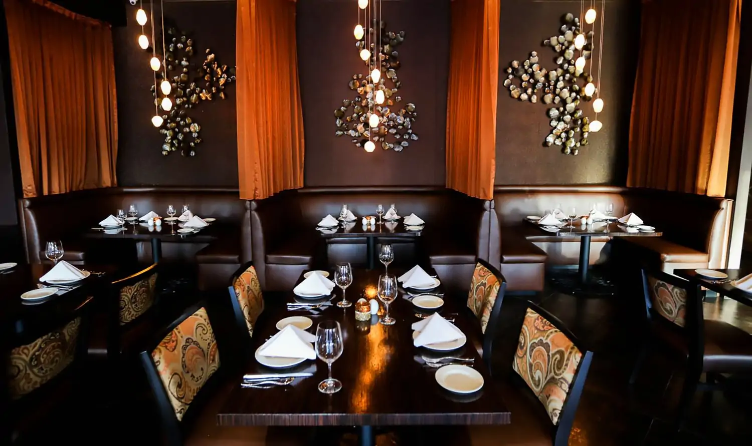 An elegant dining room filled with modern chandeliers, dark espresso leather booths, and upholstered dining chairs around dark wood tables at Spice Affair, one of the top Indian restaurants in Los Angeles on OpenTable.