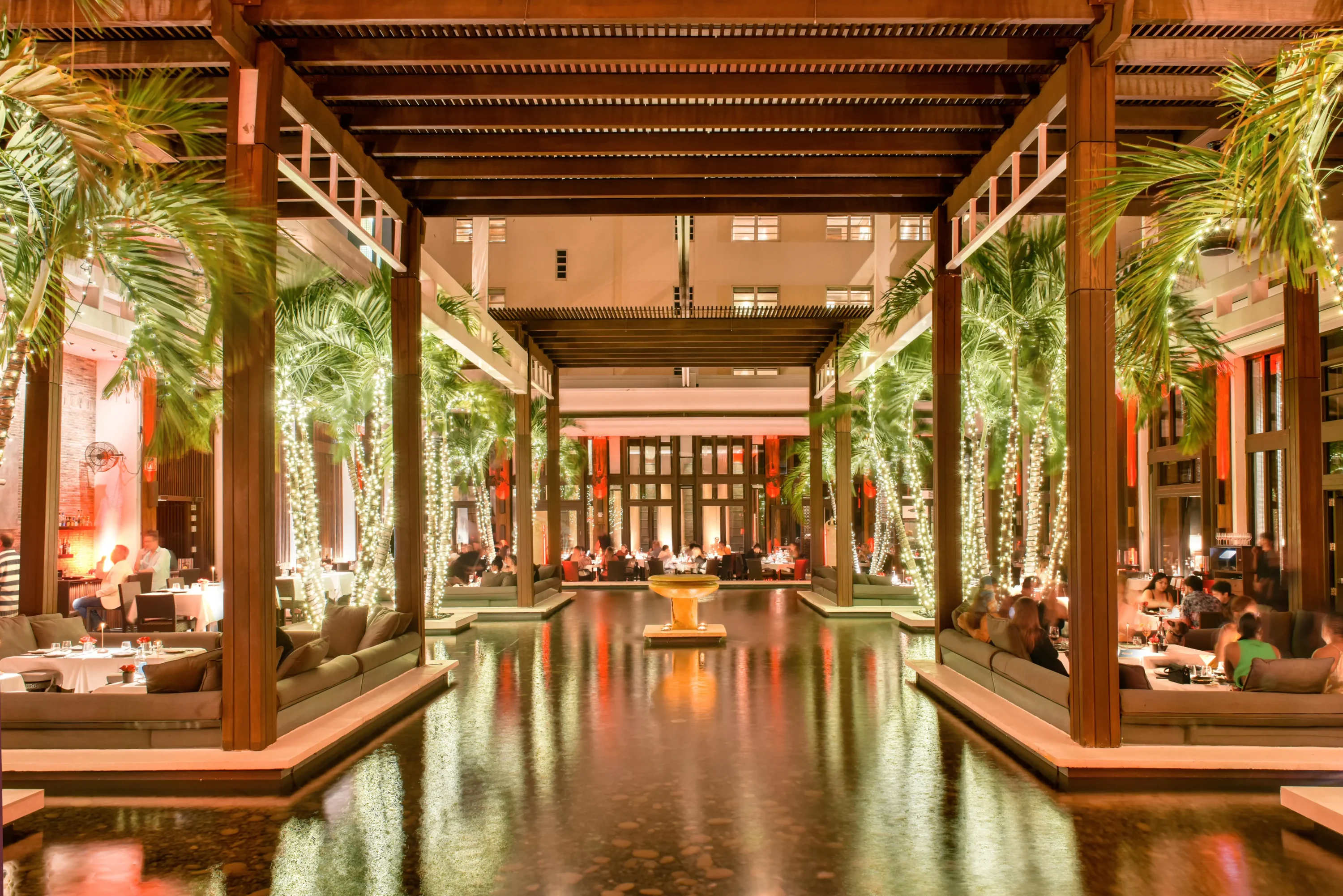 A spacious outdoor lounge with sunken seating, palm trees wrapped with string lights, and a pool at Jaya at The Setai, one of the best restaurants in Miami Beach, on OpenTable.