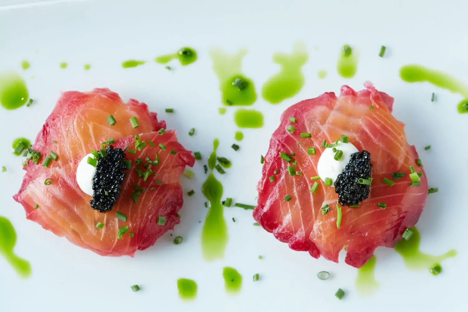 Cured salmon topped with crème fraiche and American caviar is drizzled with green sauce on a white plate at Bistro 31 at Park Cities, an Open Table selection and one of the best lunch restaurants in Dallas.