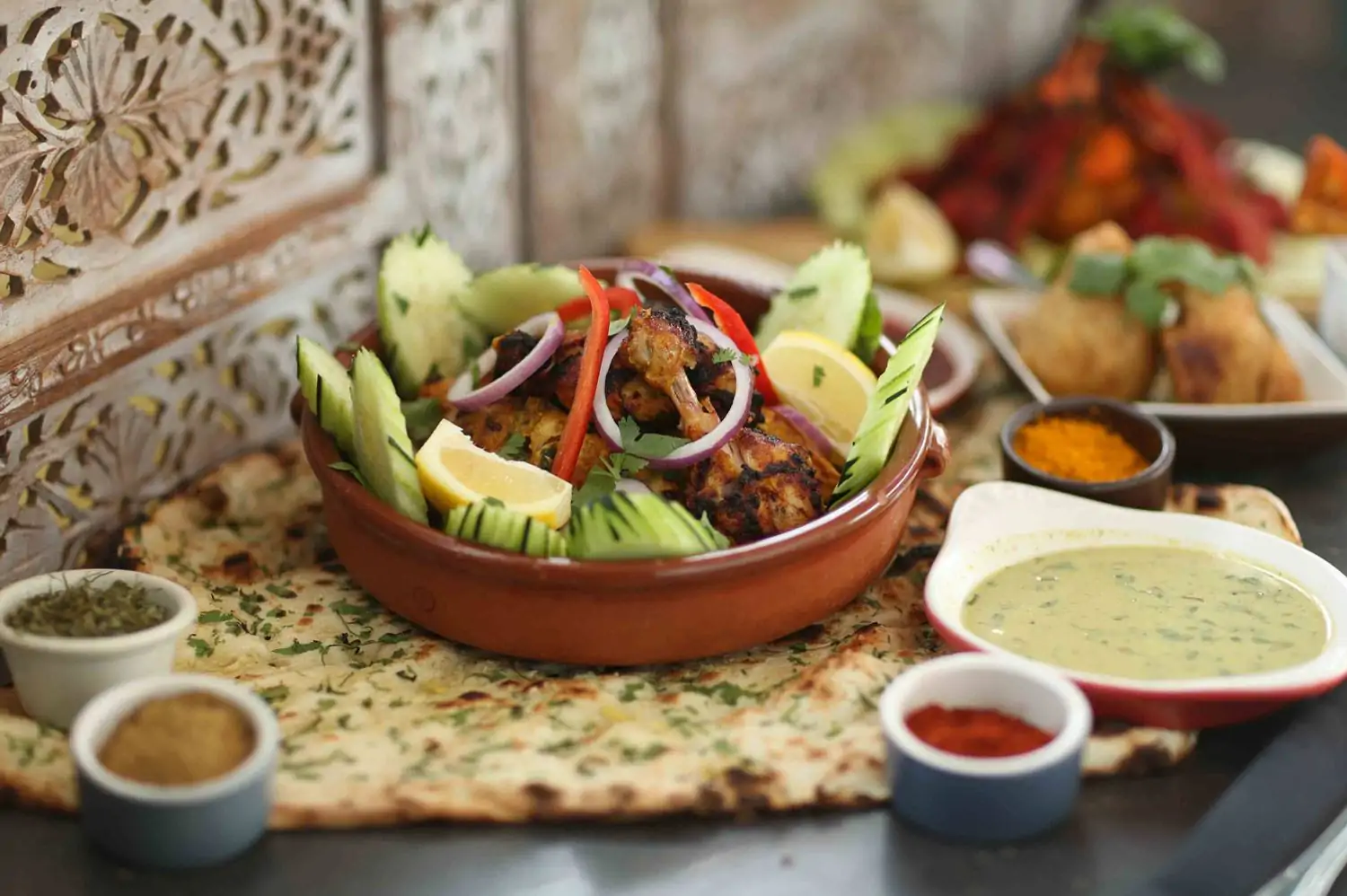 A small clay dish filled with tandoori chicken and fresh cucumber garnish rests on a bed of fresh naan bread at Radhika, one of the best Indian restaurants in Los Angeles, available to book on OpenTable.