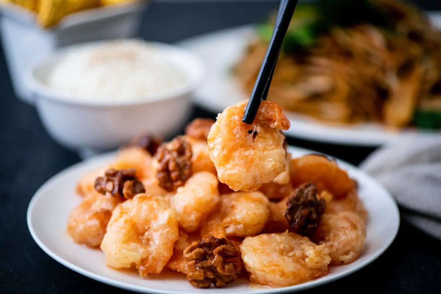 A plate with fried breaded shrimp and walnuts with a pair of chopsticks holding a piece of shrimp above the plate at Panda Inn, a Chinese restaurant in Los Angeles specializing in regional food bookable on OpenTable.