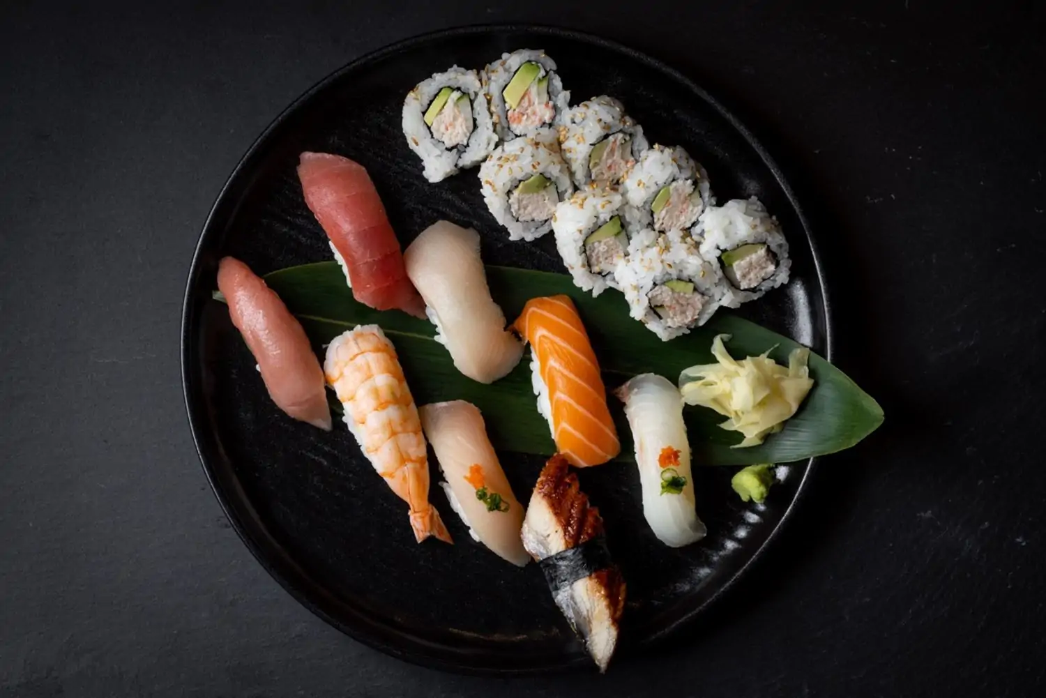 A variety of sushi rolls and nigiri arranged on a black plate, including tuna, salmon, shrimp, eel, and California rolls at Katsuya in Los Angeles, which you can book on OpenTable.