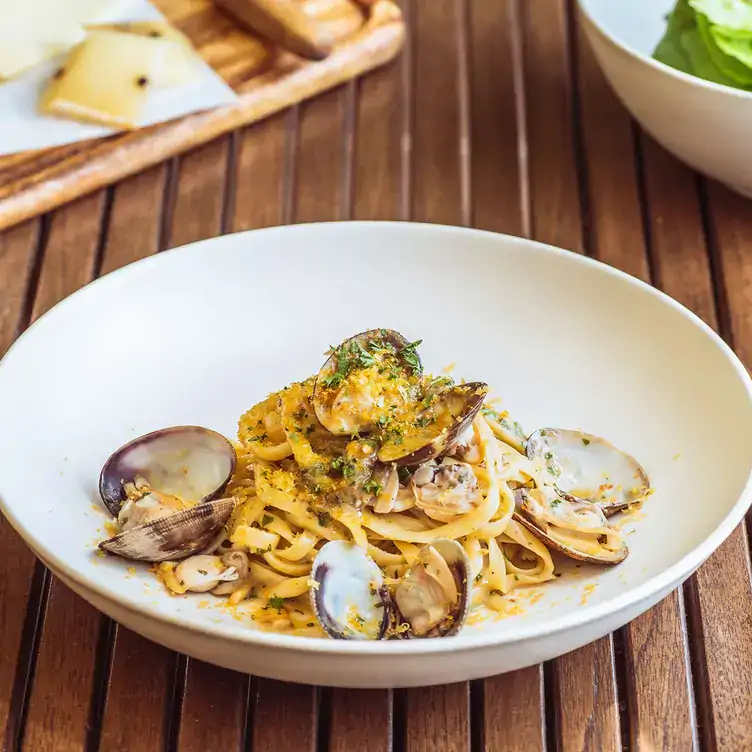 A plate of linguine pasta with clams, topped with fresh herbs and lemon zest atop a wooden slat table at L'Antica Pizzeria Da Michele, one of the best Los Angeles Hollywood restaurants you can reserve ahead on OpenTable.