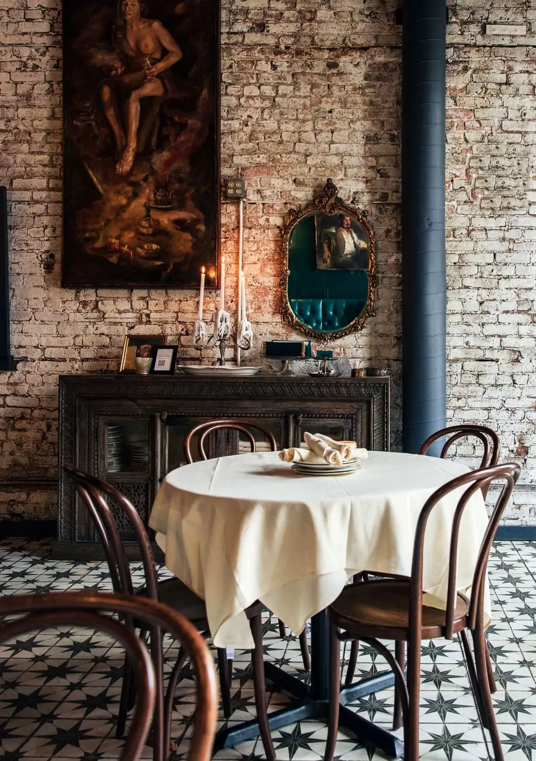 A table setting with a white tablecloth and cloth napkins in front of a painted brick wall, candles, and classical art in the background at Elina’s, one of the best cozy restaurants in Chicago, found on OpenTable.